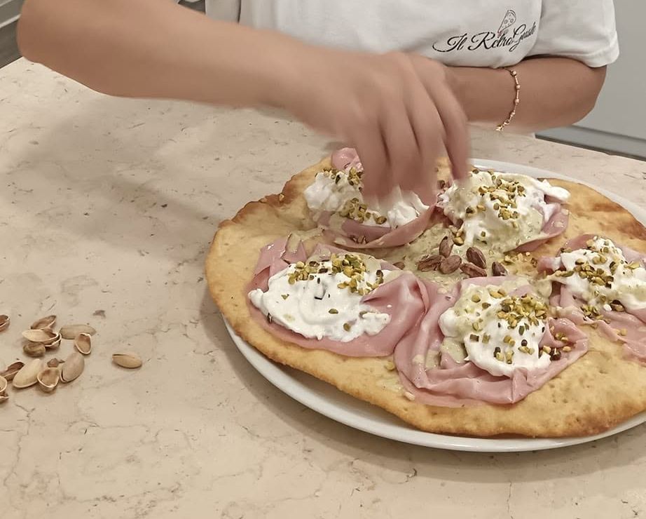 Mani che condiscono un ciccio con mortadella, stracciatella e pistacchio