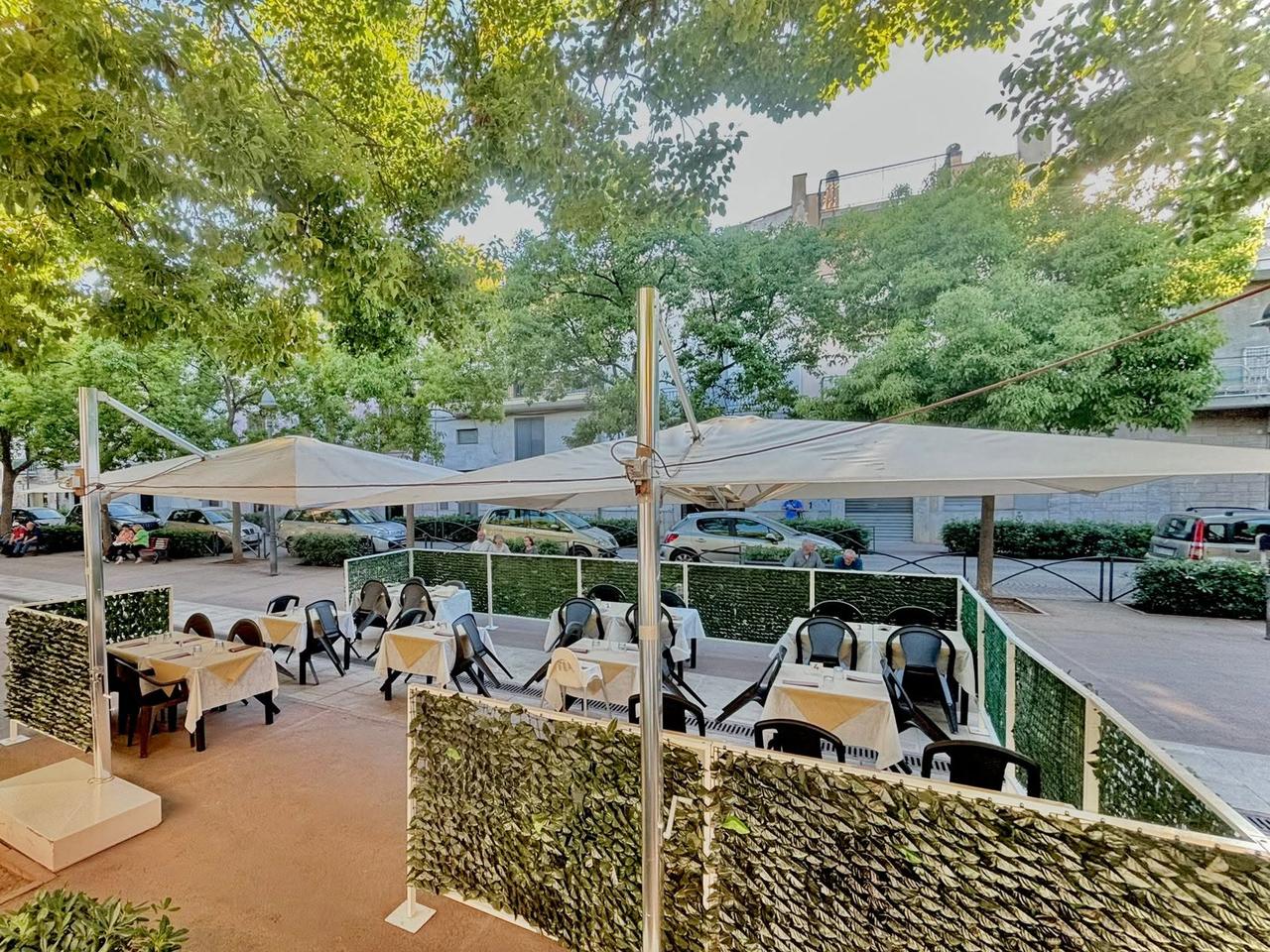 I tavoli all'aperto del Retrogusto, sotto gli ombrelloni e gli alberi della piazza