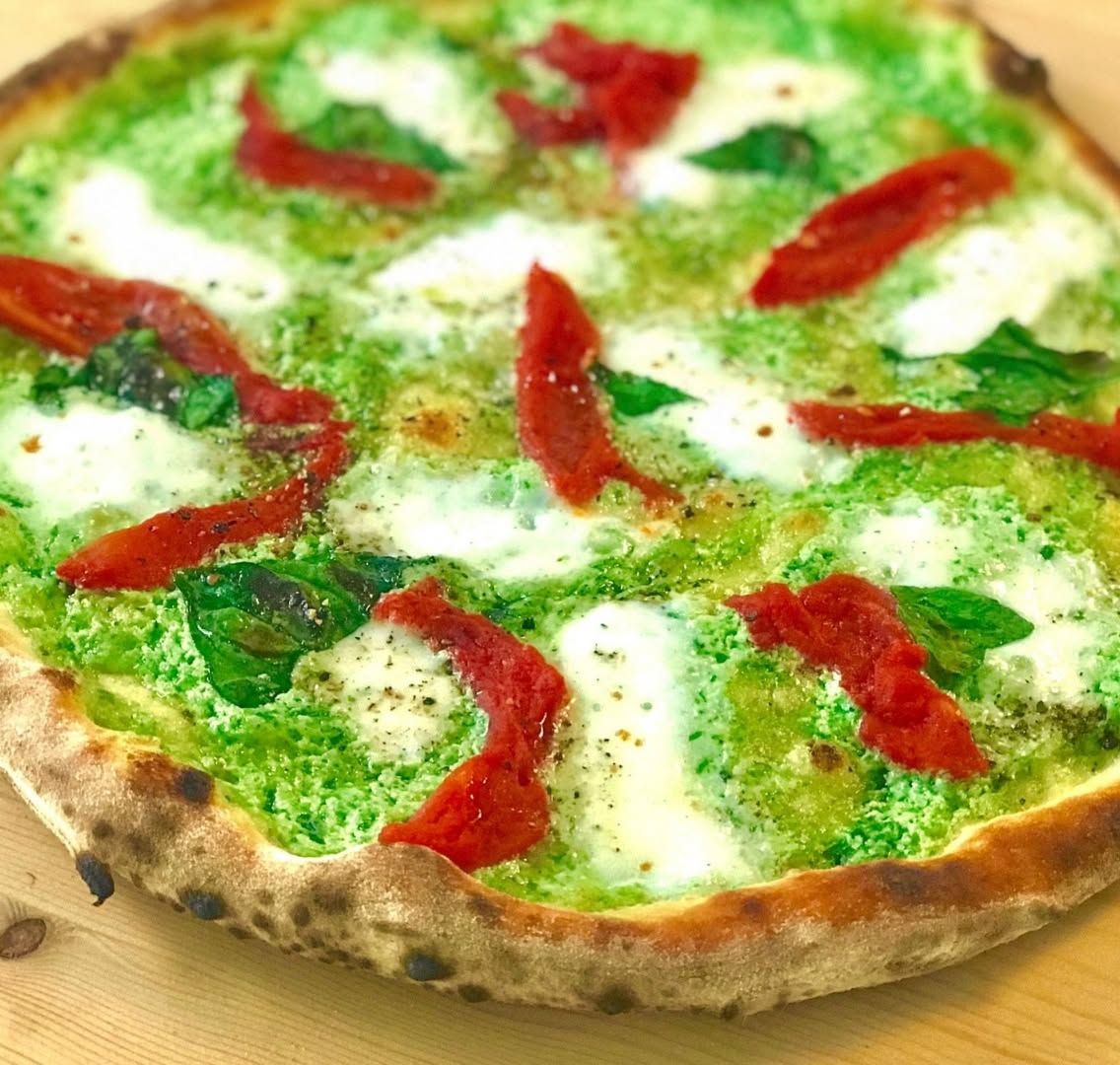 Pizza appena sfornata con crema verde, mozzarella e foglie di basilico